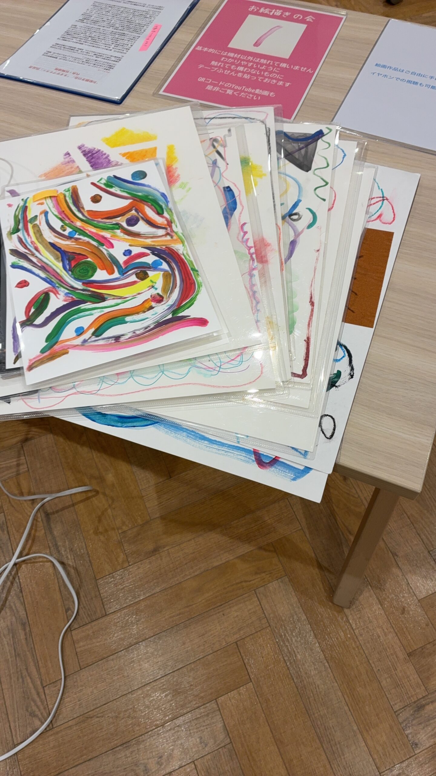 JamJam展で出品の準備をした写真。初出品のためもあり、また大量の紙作品の展示のため、きれいに並べるスペースはなく、クリアケースのようなものに入れて扇状に重ねて置いてある。ケースに入れられないものは、紙のまま。自分でも雑だと思うものの、作品への愛着の持ち過ぎへの反抗心の現れでもあったかもしれない。